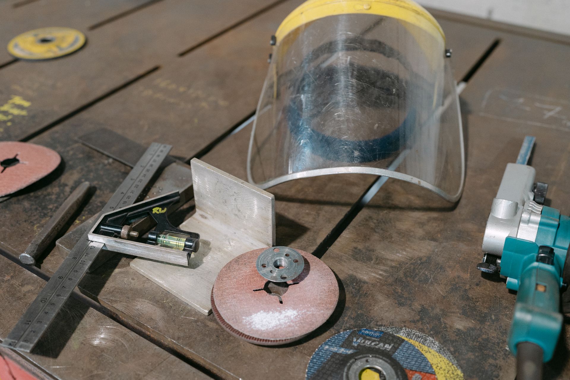 Clear face shield and tools on a wooden workbench, including sanding discs and metal parts