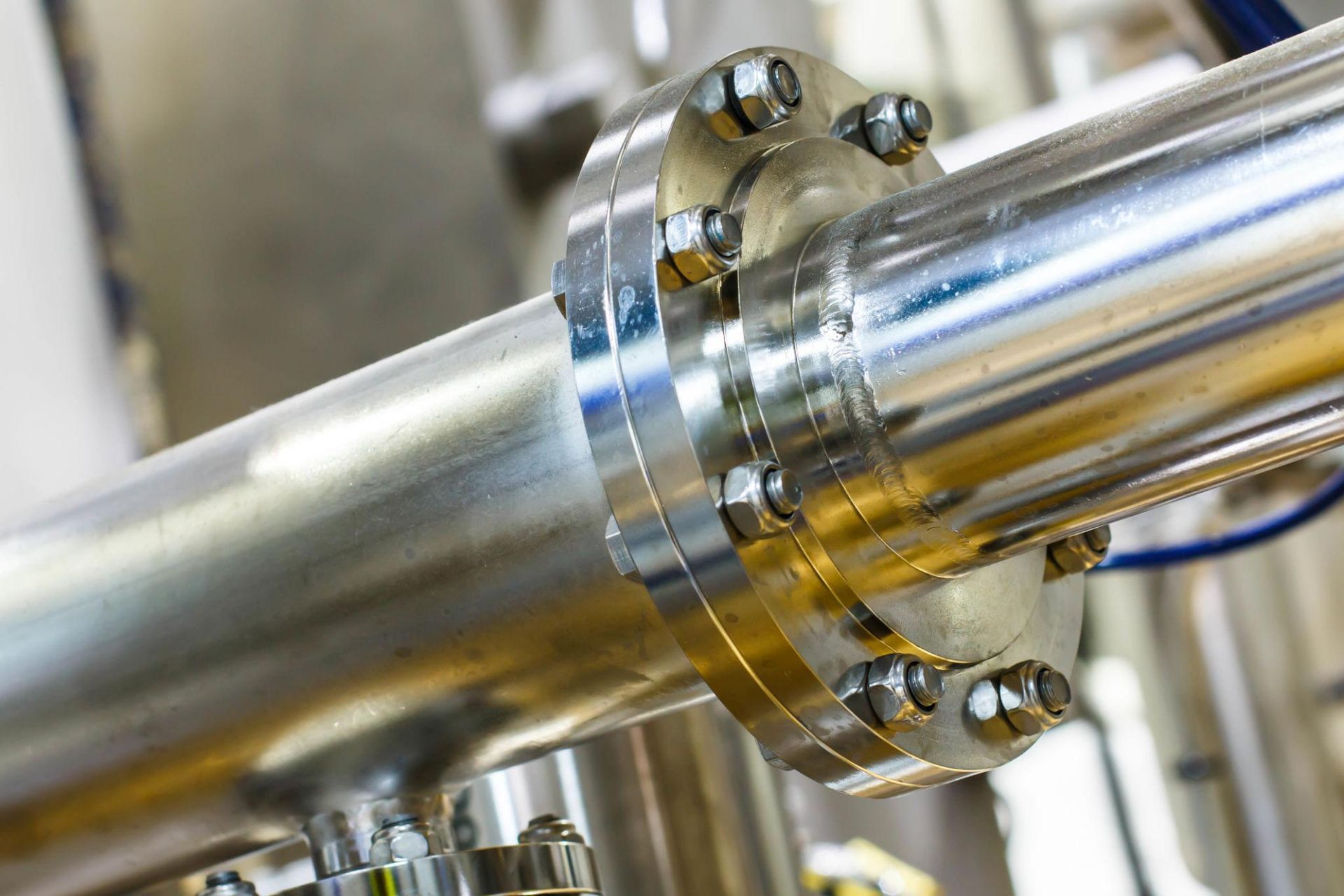Close-up of shiny metal pipes joined by a bolted stainless steel flange in an industrial setting