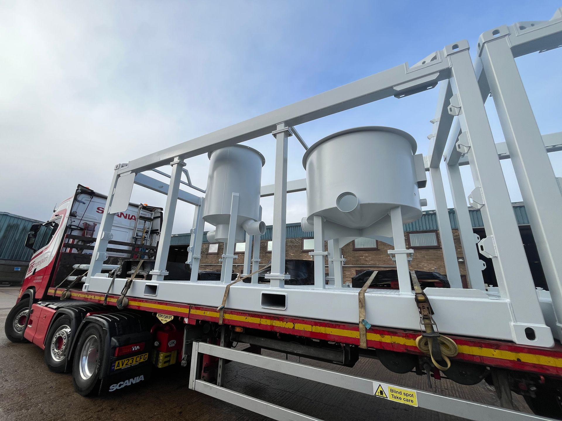 White industrial tanks loaded on a flatbed truck under a cloudy sky