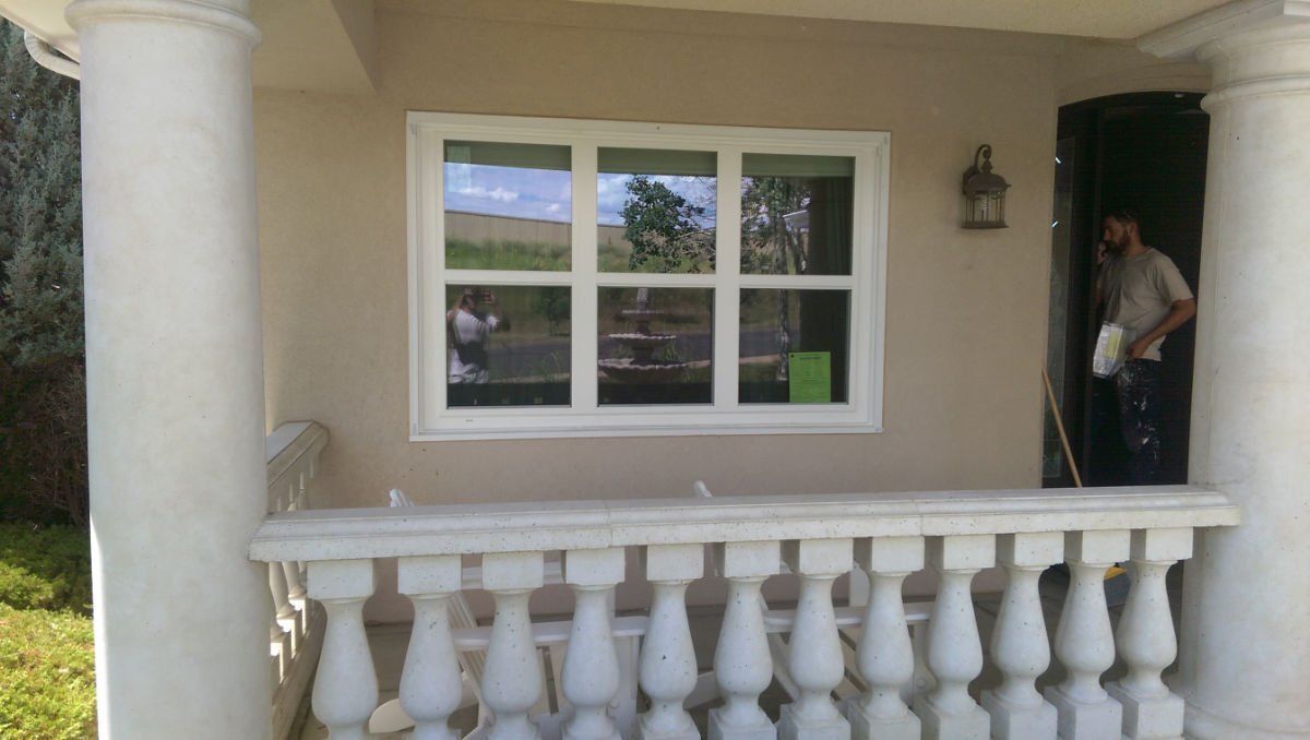A man is standing on a porch next to a window.