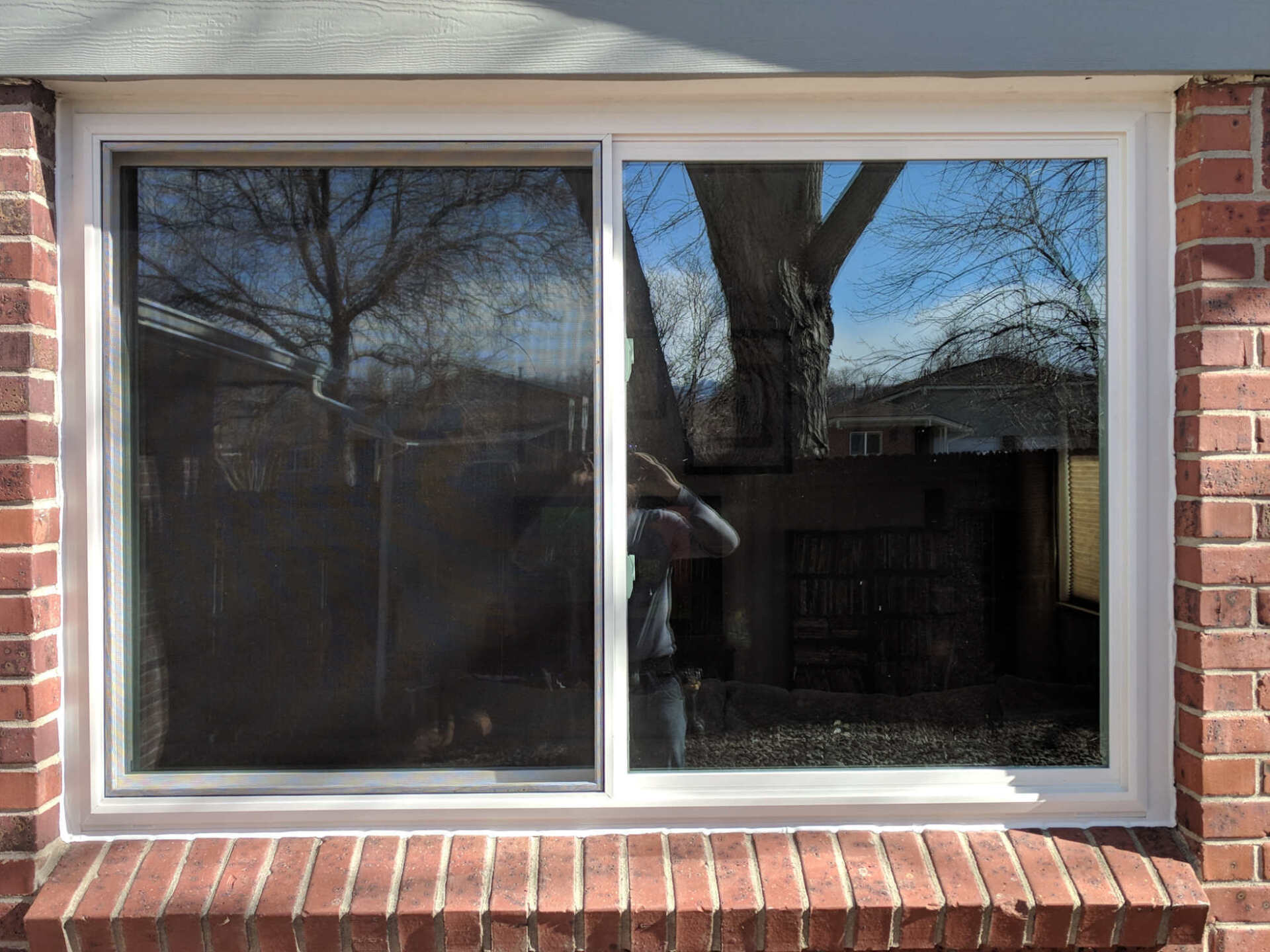 A white window with a sliding glass door is on a brick wall.
