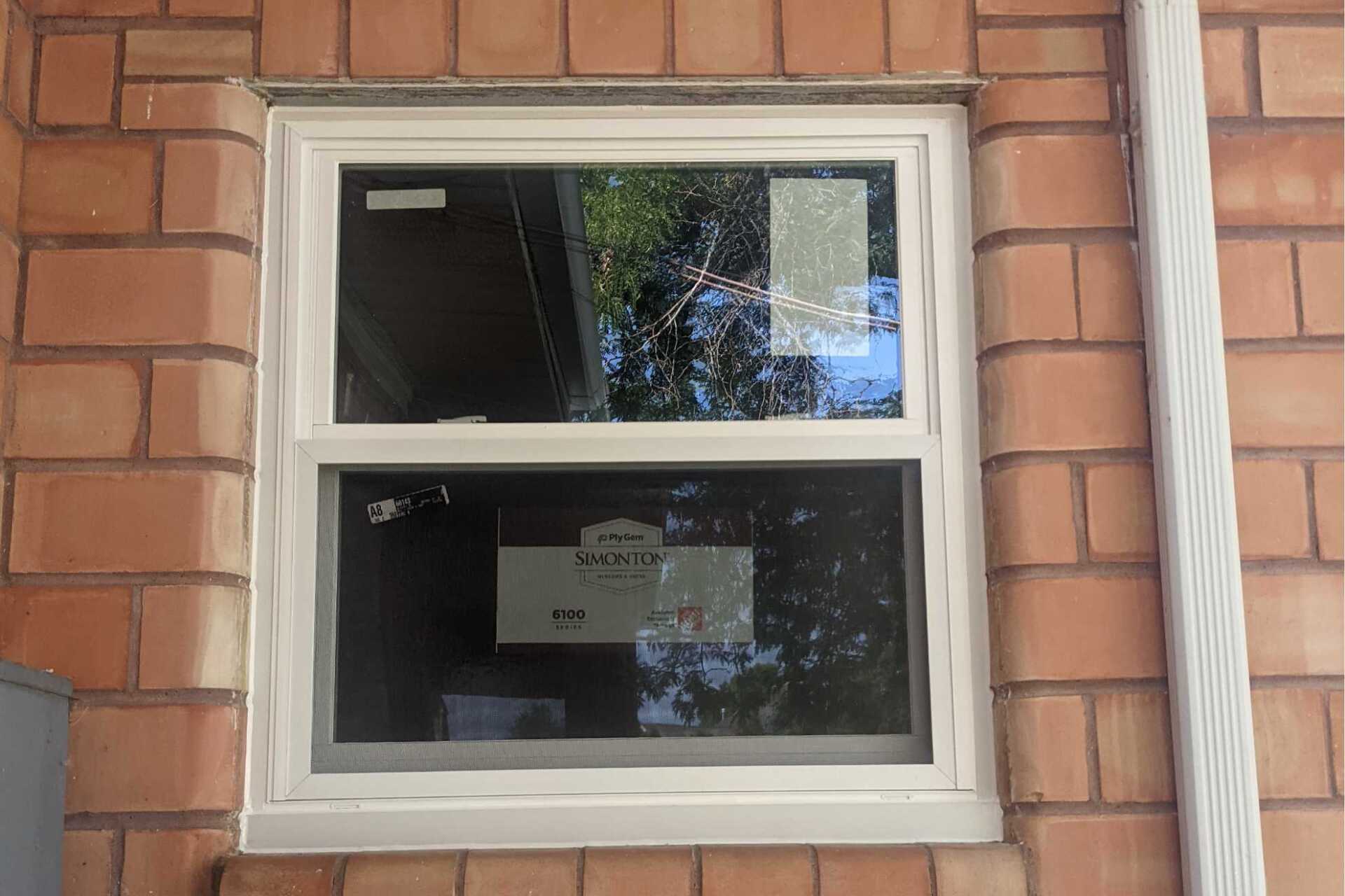 A white window is sitting on a brick wall.