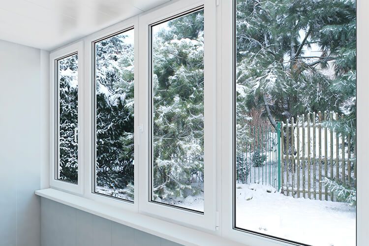 A room with a lot of windows looking out to a snowy forest.
