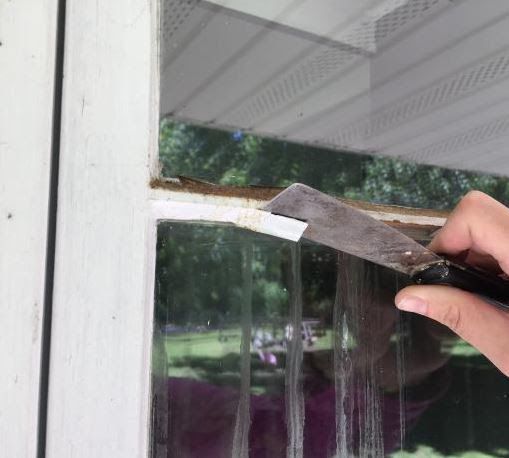 A person is using a spatula to remove paint from a window.