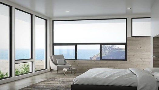 A bedroom with a bed , chair , and lots of windows overlooking the ocean.