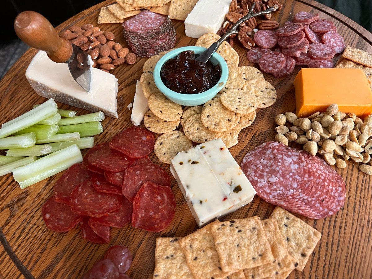 A wooden cutting board topped with crackers , cheese , salami , nuts and celery.