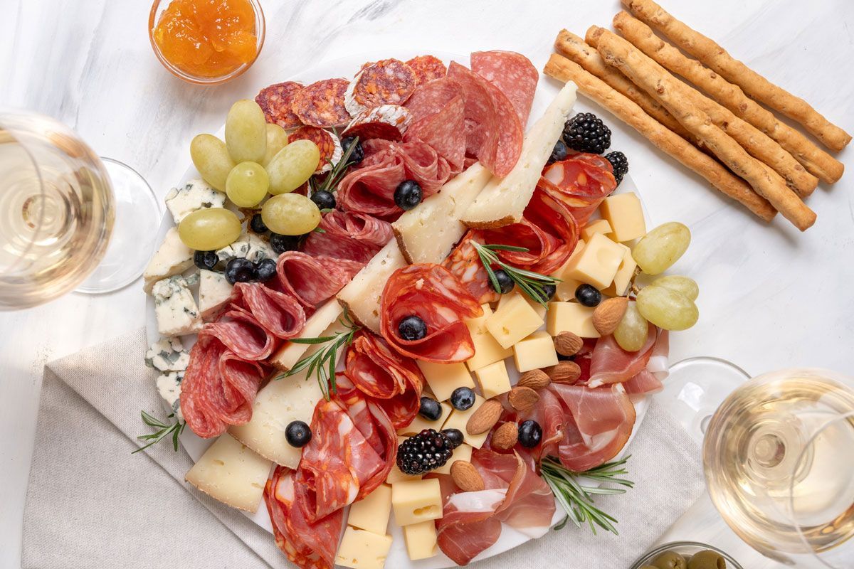 A white plate topped with meat , cheese , grapes , and crackers.