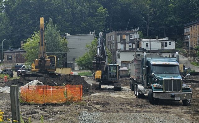 Construction site with excavators and a dump truck on muddy ground near a wooded hillside