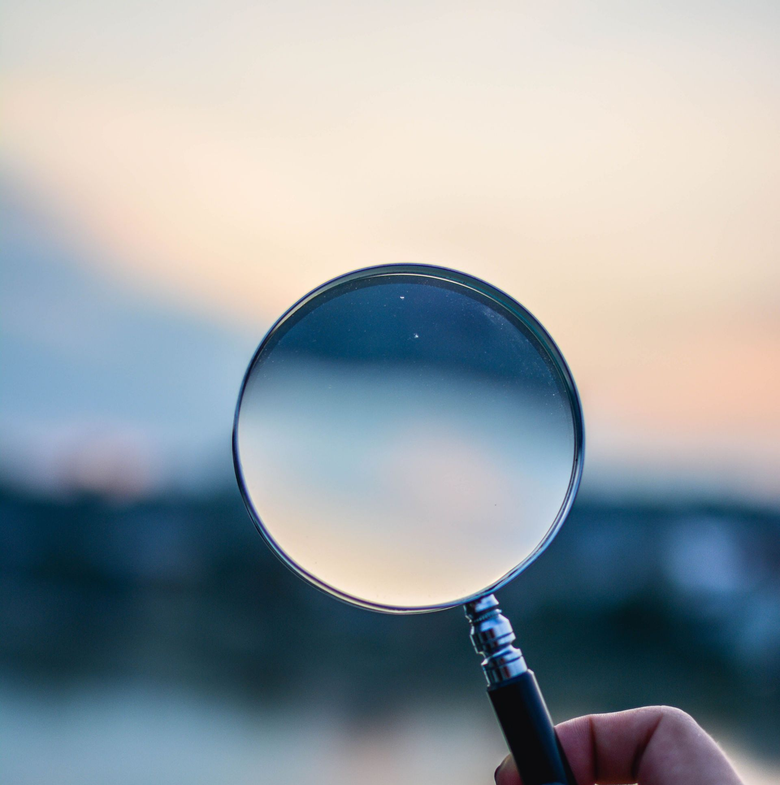 Hand holding a magnifying glass against a blurred sunset sky