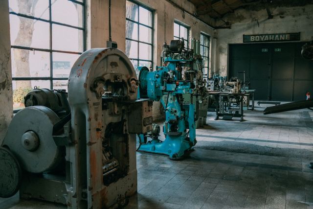 Abandoned industrial workshop with teal machinery and large windows, lit by soft daylight