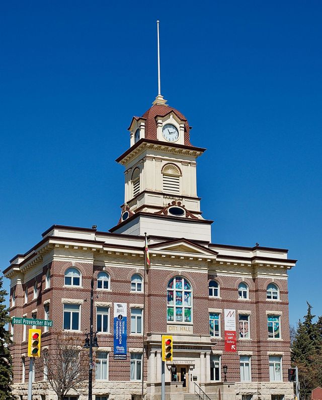 Historic clock tower on a brick building under a clear blue sky, with streetlights in front.