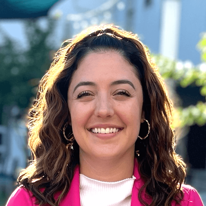 A woman wearing a pink jacket and hoop earrings is smiling for the camera.