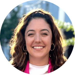 A woman wearing hoop earrings and a pink jacket smiles for the camera