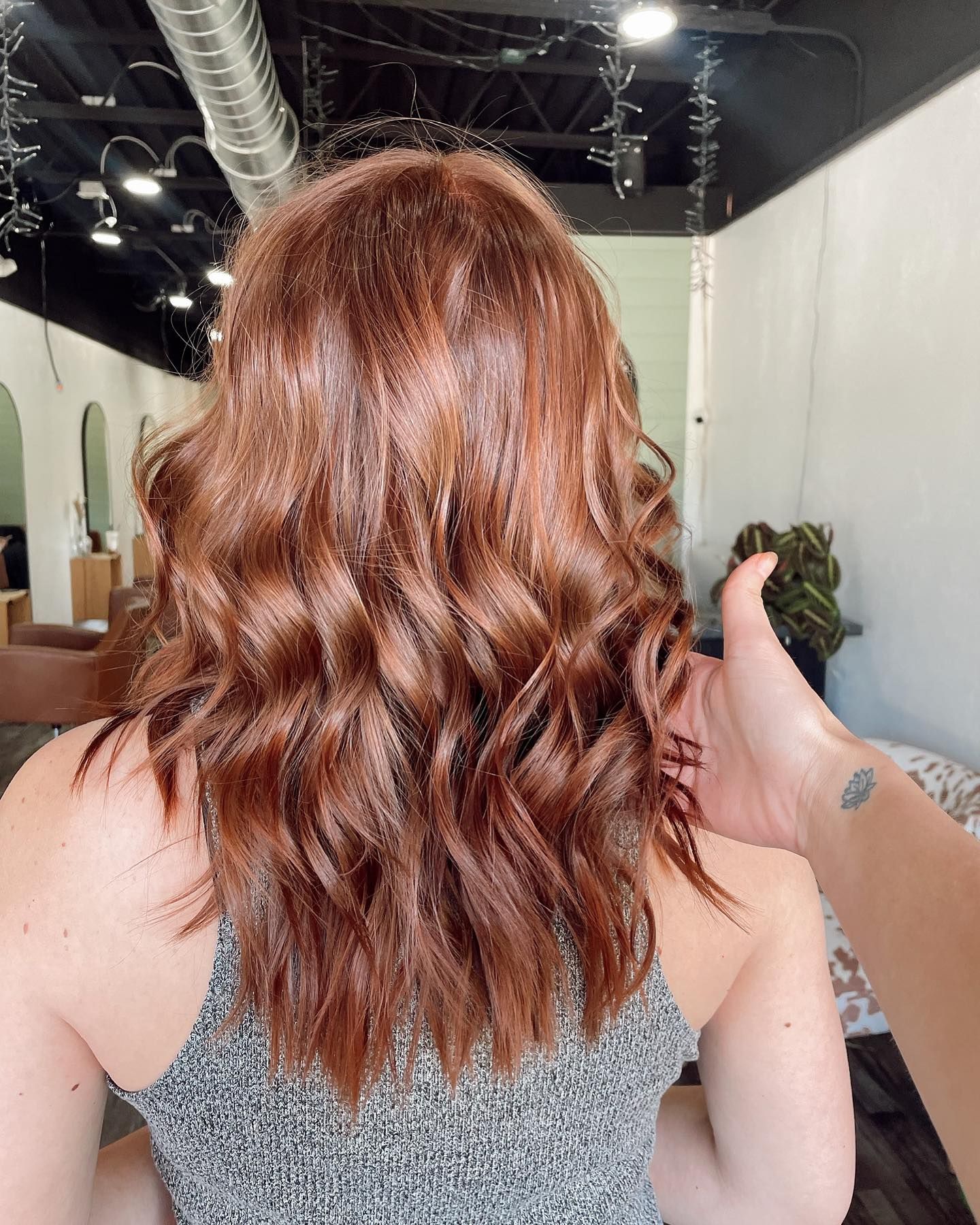 Woman with wavy, reddish-brown hair in a salon; a hand touches the hair from the side.