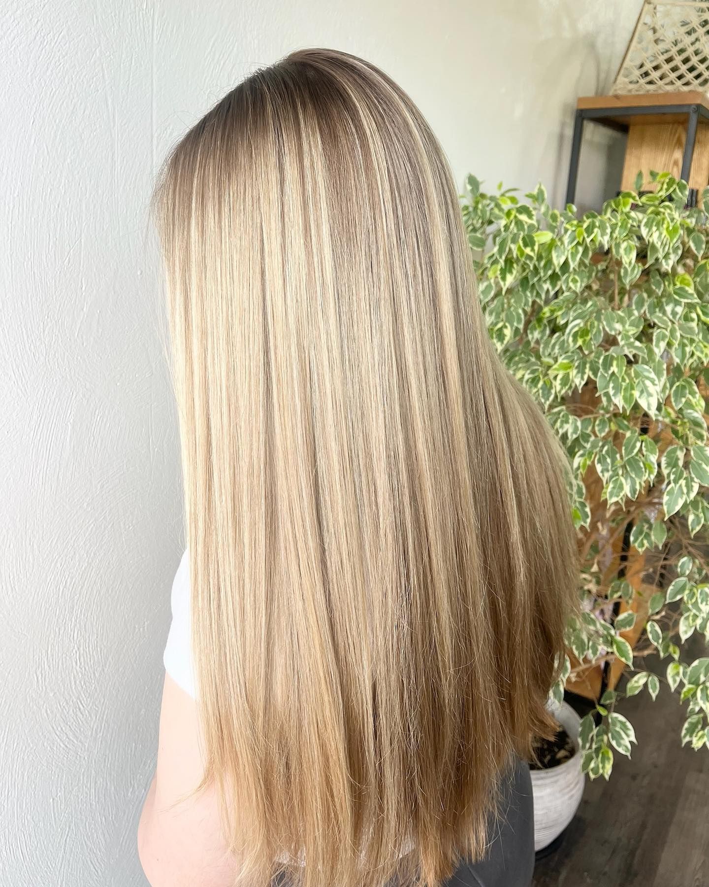 Blonde crimped hair with ombre effect; next to a white wall and a plant in a pot.