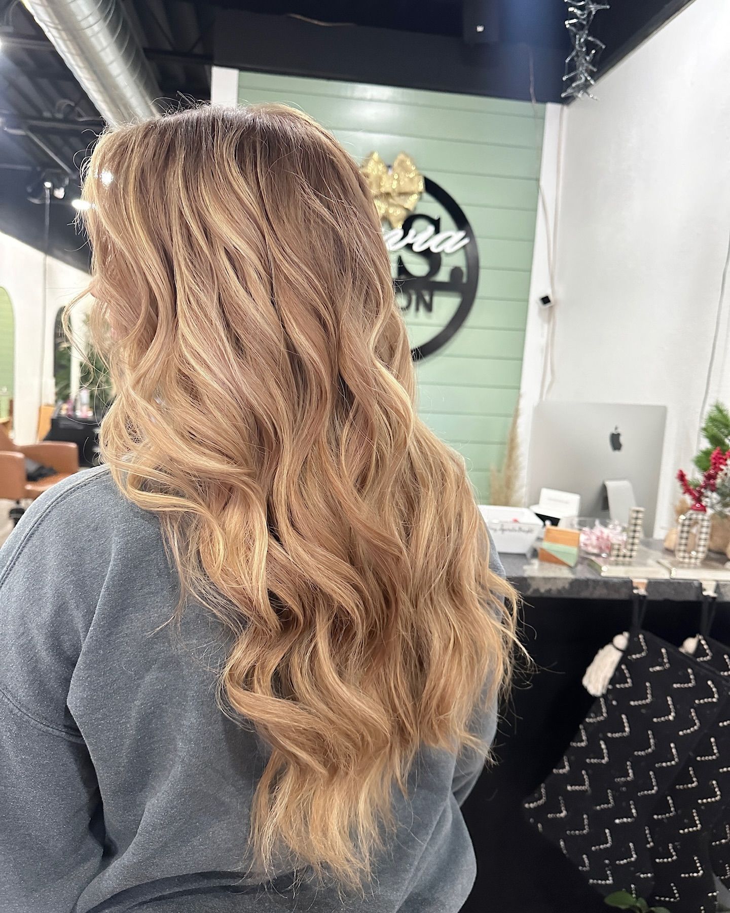 Woman with long, wavy blonde and brown highlighted hair; salon interior in background.