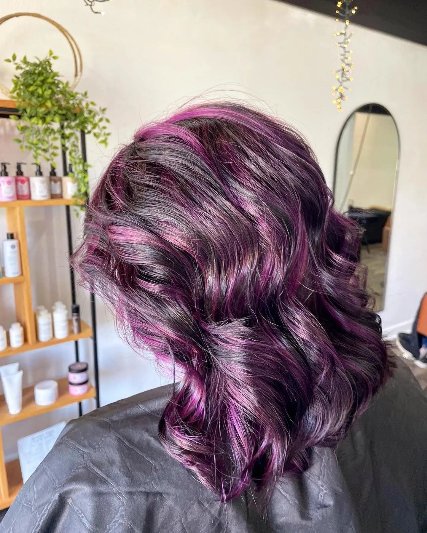 Short wavy hair dyed purple-black with pink highlights, shown from the back in a salon chair.