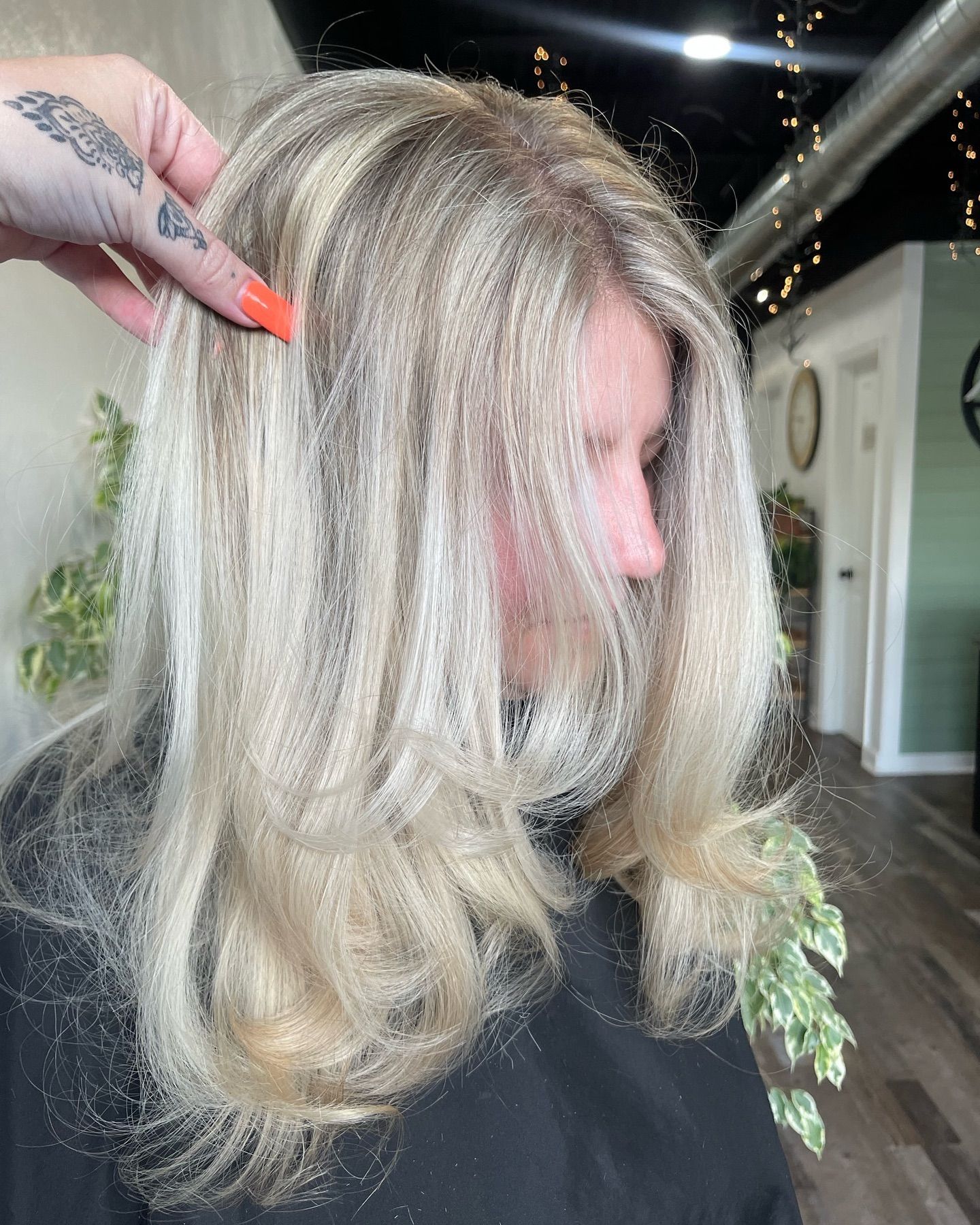 Blonde hair styled with highlights, a hand touches the hair. In a salon setting.
