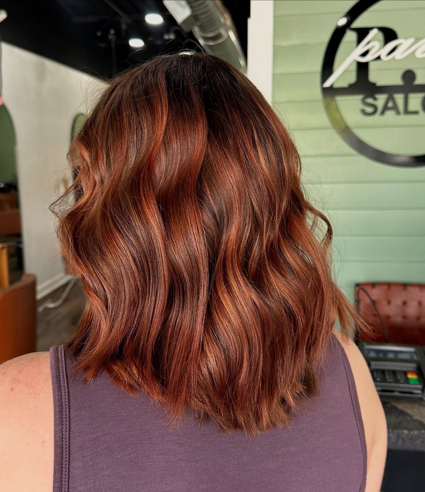 Woman with shoulder-length, reddish-brown wavy hair. The salon is in the background.