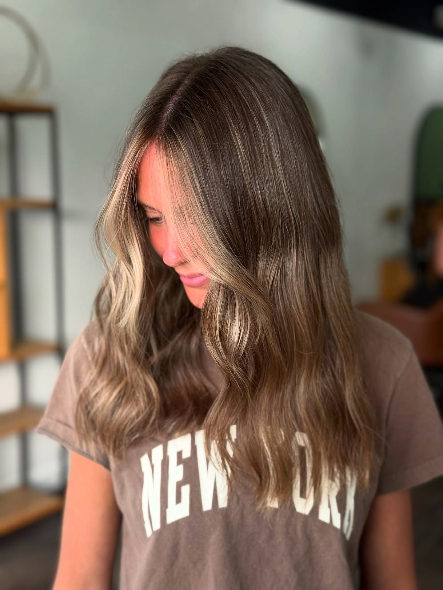 Woman with long, wavy brown hair with blonde highlights; wearing a brown 