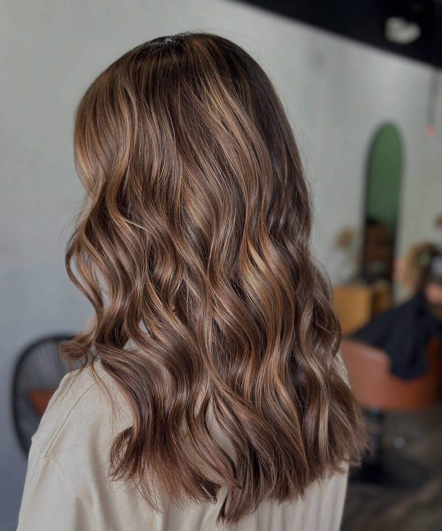 Shoulder-length, wavy brown hair with subtle highlights, viewed from behind in a salon setting.