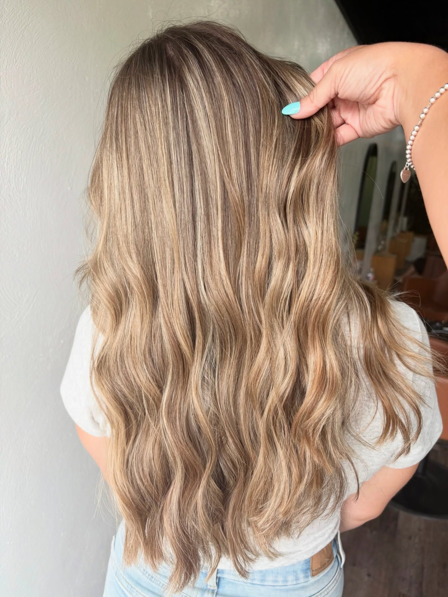 Long wavy blonde hair with highlights, being touched by a hand with turquoise nails.
