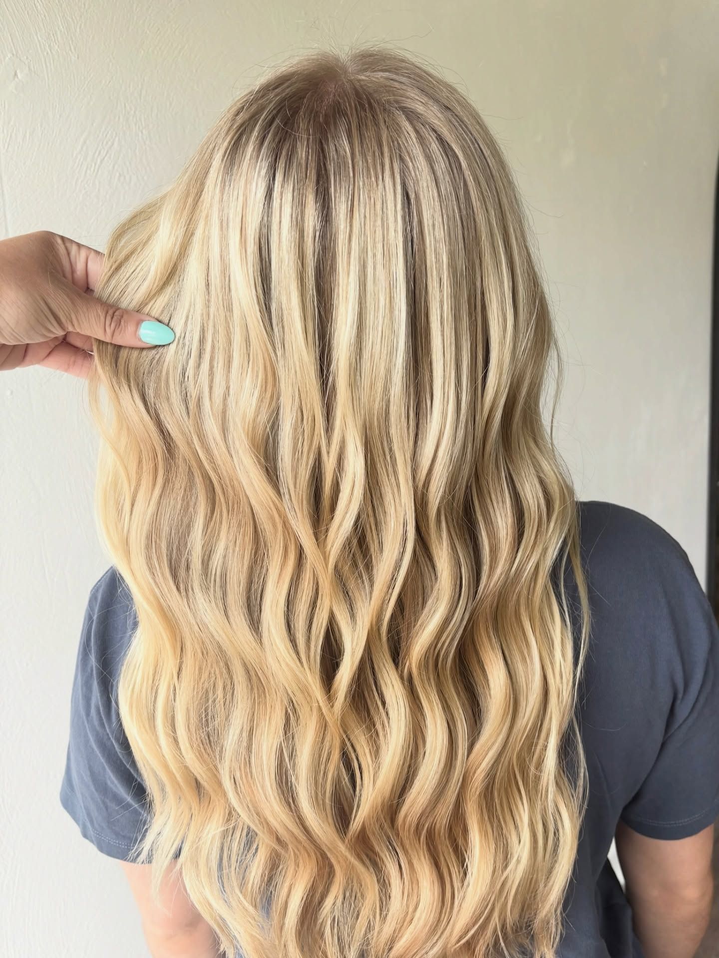 Blonde hair with wavy texture, held by a hand with turquoise nail polish.