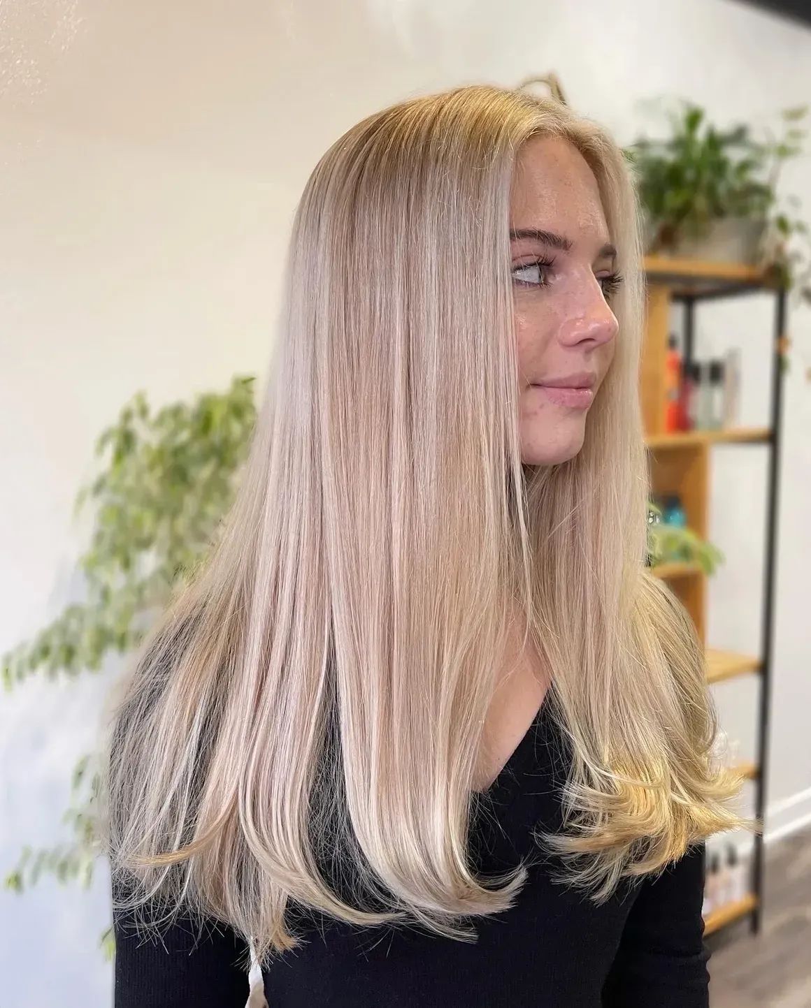 Profile view of a woman with straight blonde hair in a bright room with plants and shelves