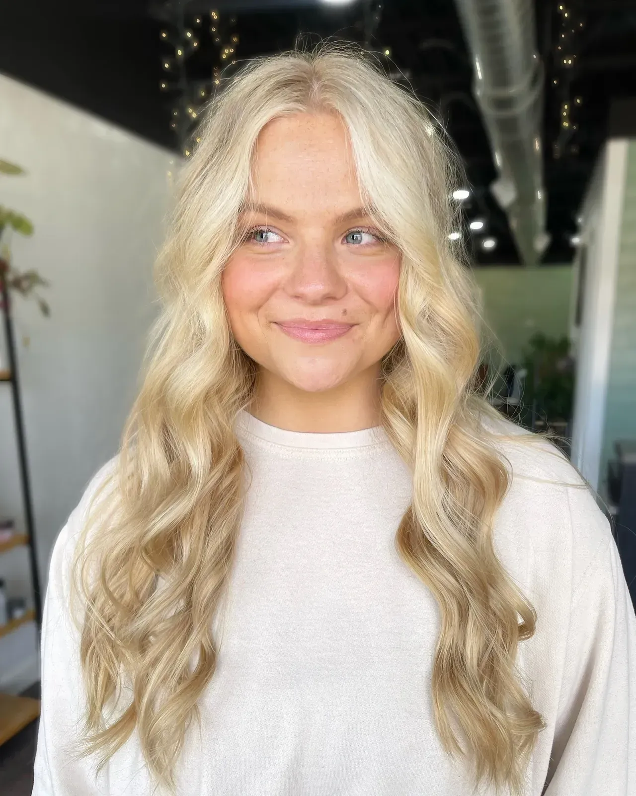 Woman with long, wavy blonde hair smiles, wearing a cream sweater.