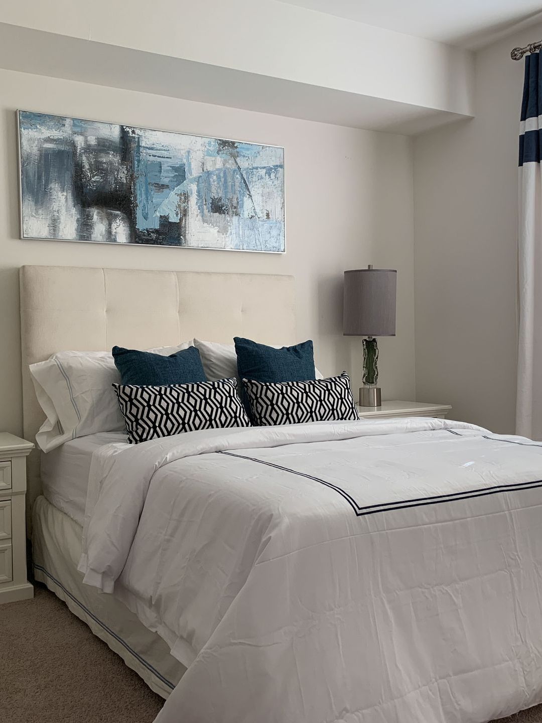 a bedroom with a bed , nightstand , lamp and painting on the wall .