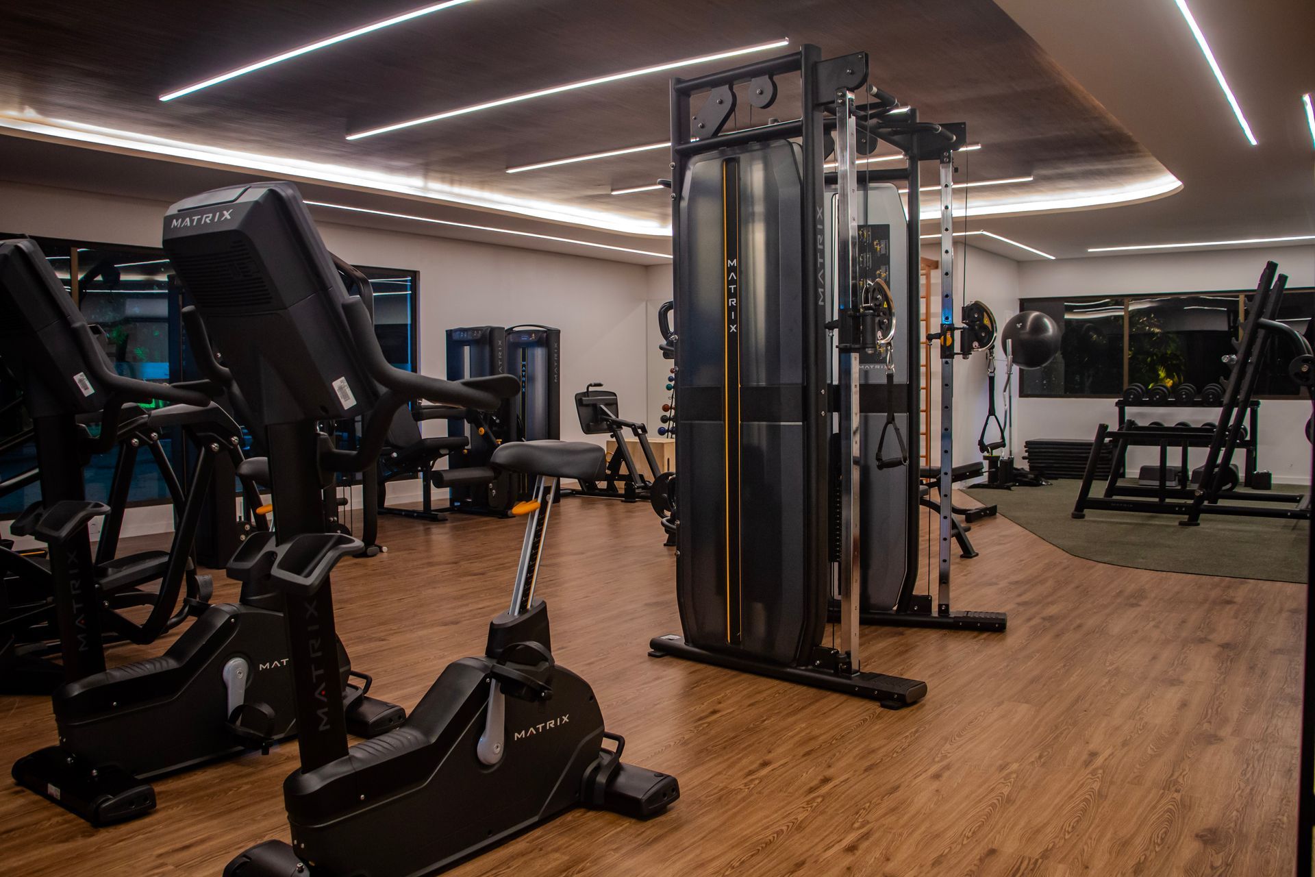 Interior de academia moderna com aparelhos de cardio, equipamentos de musculação e piso de madeira.