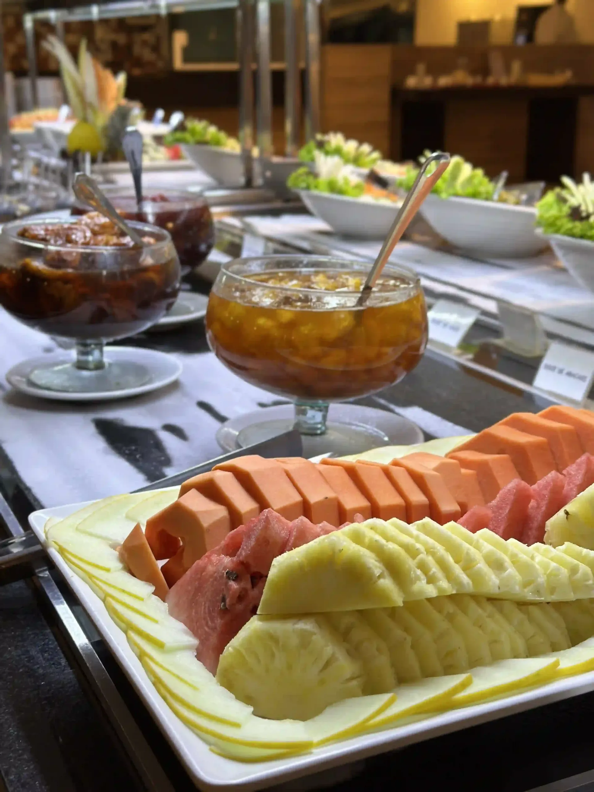 Mesa de buffet com fatias de melancia e outras fruteiras em uma mesa de jantar ensolarada.