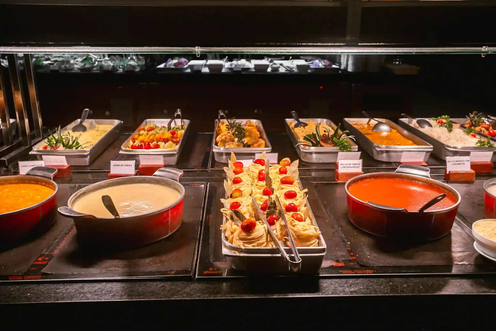 Buffet com aperitivos e sobremesas variadas em bandejas sob iluminação aconchegante.