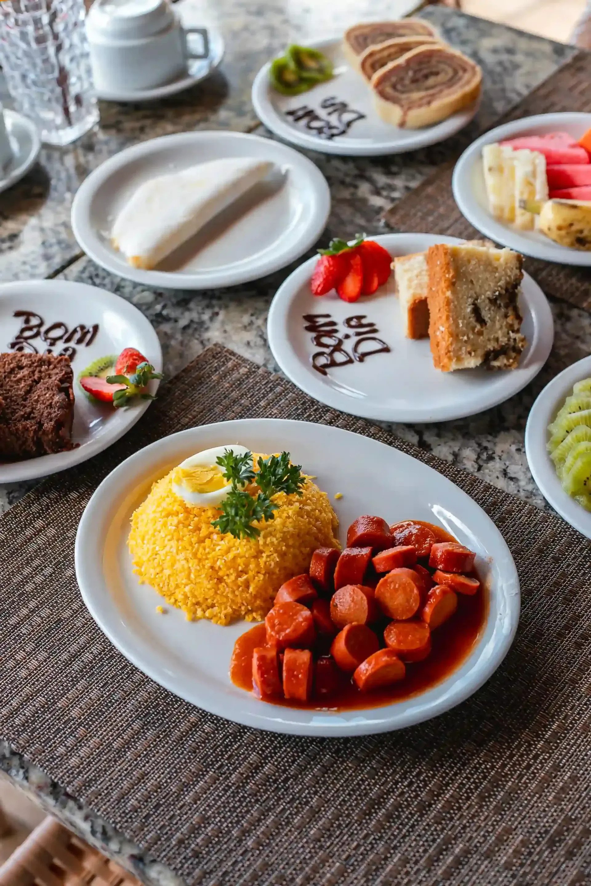 Mesa com um buffet de café da manhã contendo salsicha, ovos, torradas, frutas e café.