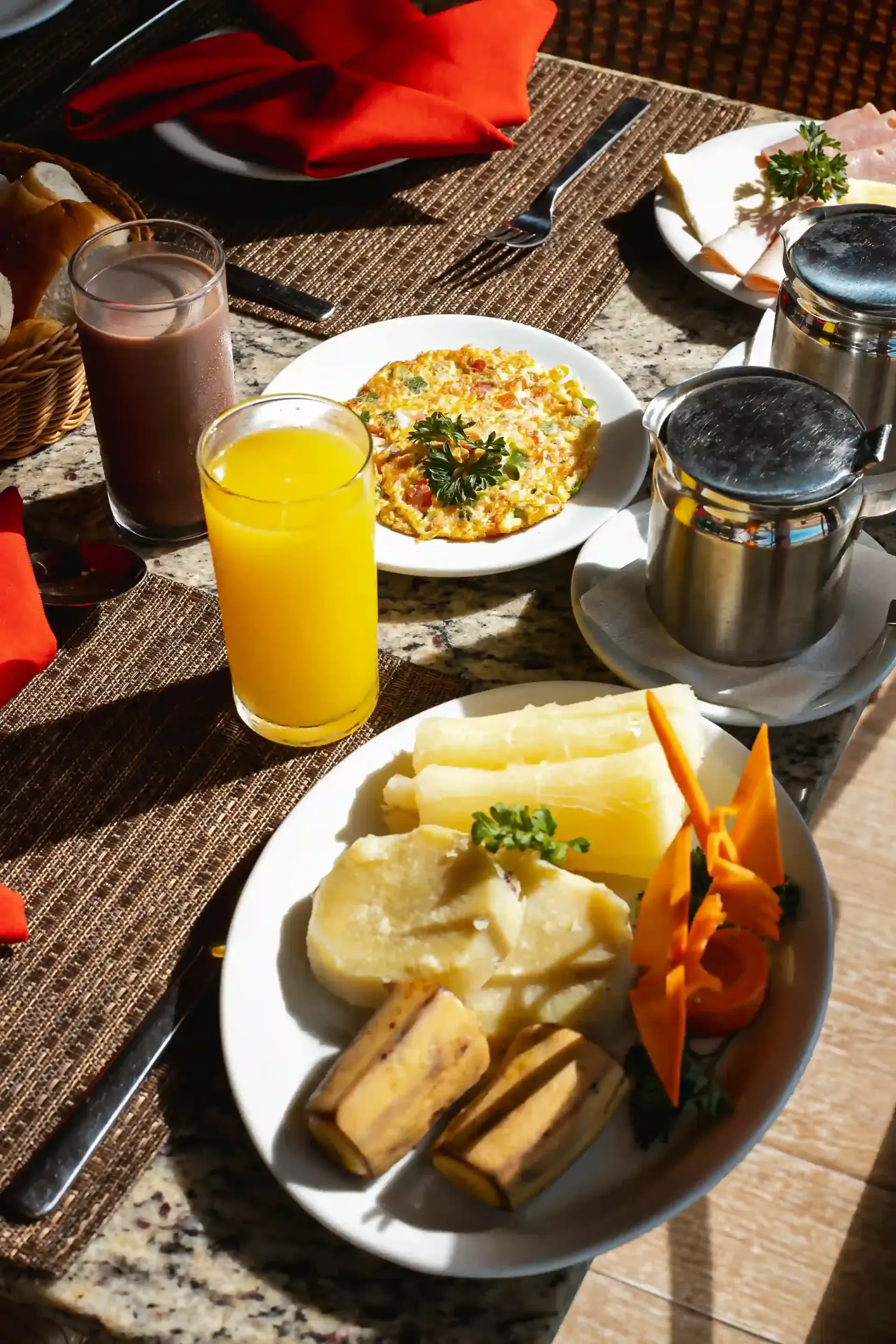 Café da manhã servido na mesa: suco, achocolatado, ovos mexidos, torradas, frutas e condimentos.