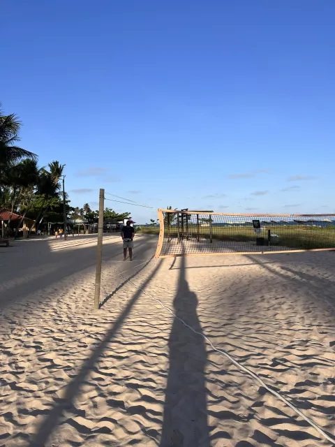 Quadra de vôlei de praia em uma praia ensolarada de areia com longas sombras e um céu azul claro.