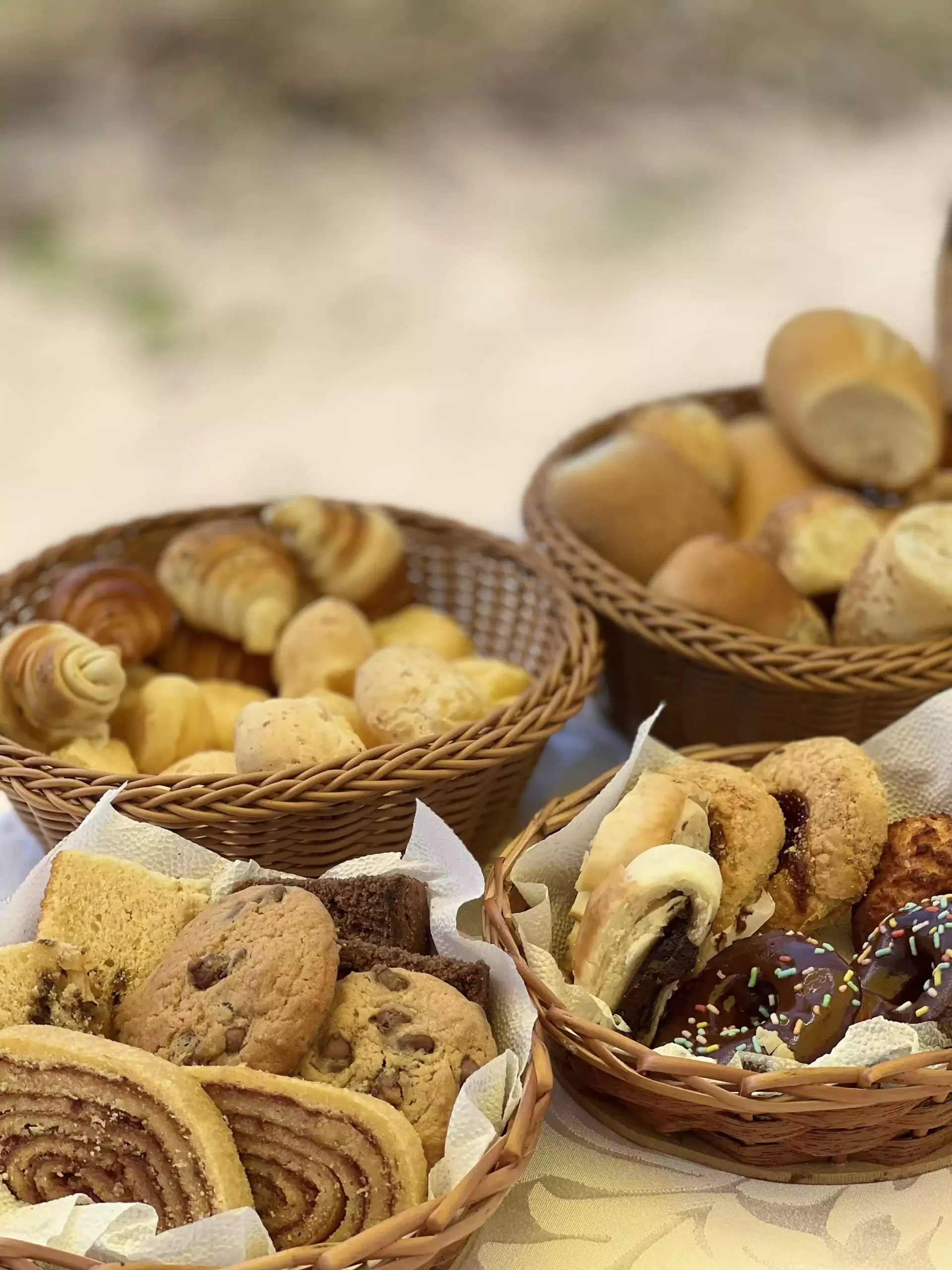 Cestas de vime variadas, repletas de biscoitos e doces, dispostas sobre uma mesa.