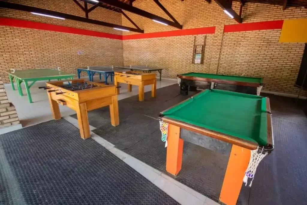 Pequena sala de recreação interna com várias mesas de bilhar, incluindo uma mesa com feltro verde na frente.