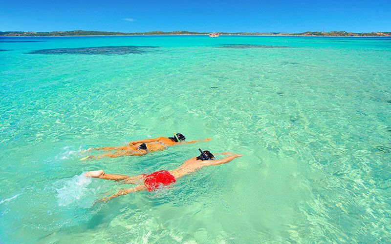 Dois mergulhadores nadando em águas tropicais cristalinas e turquesas sob um céu azul.