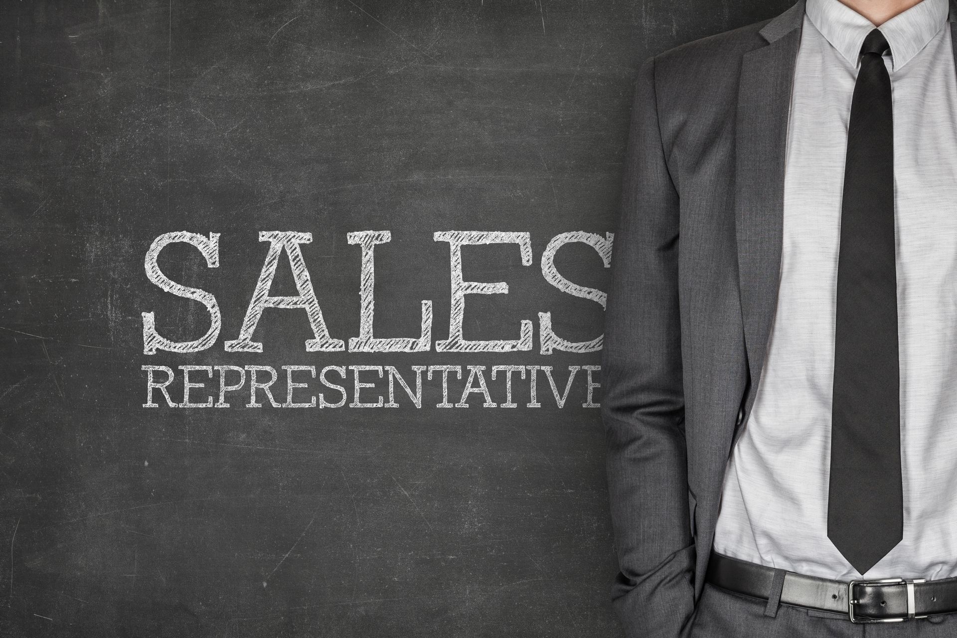 A person in a gray suit and black tie stands before a chalkboard with the words
