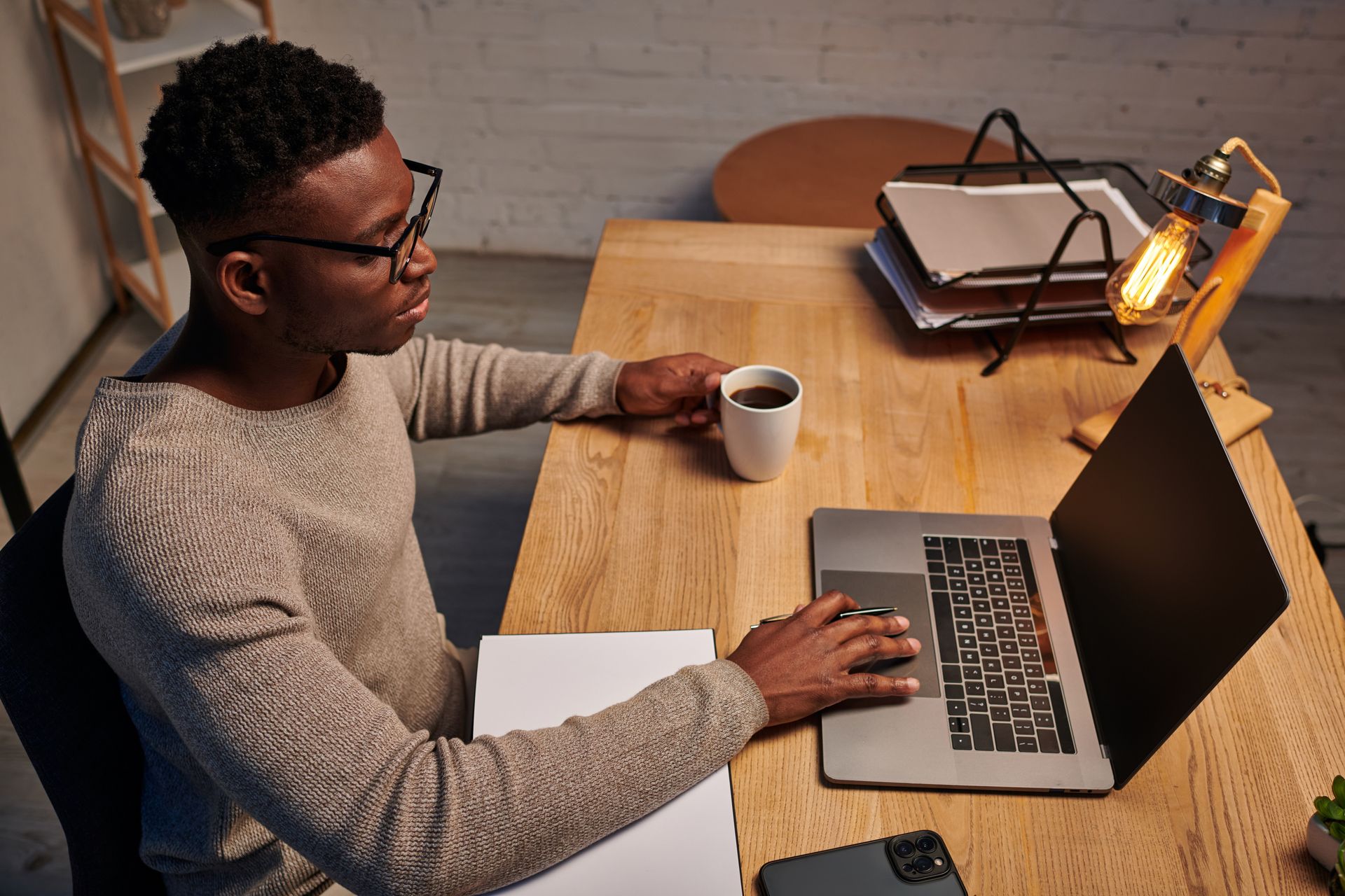 Person working at a wooden desk with laptop, notebook, and cup of coffee. Person working at a wooden desk with laptop, notebook, and cup of coffee.