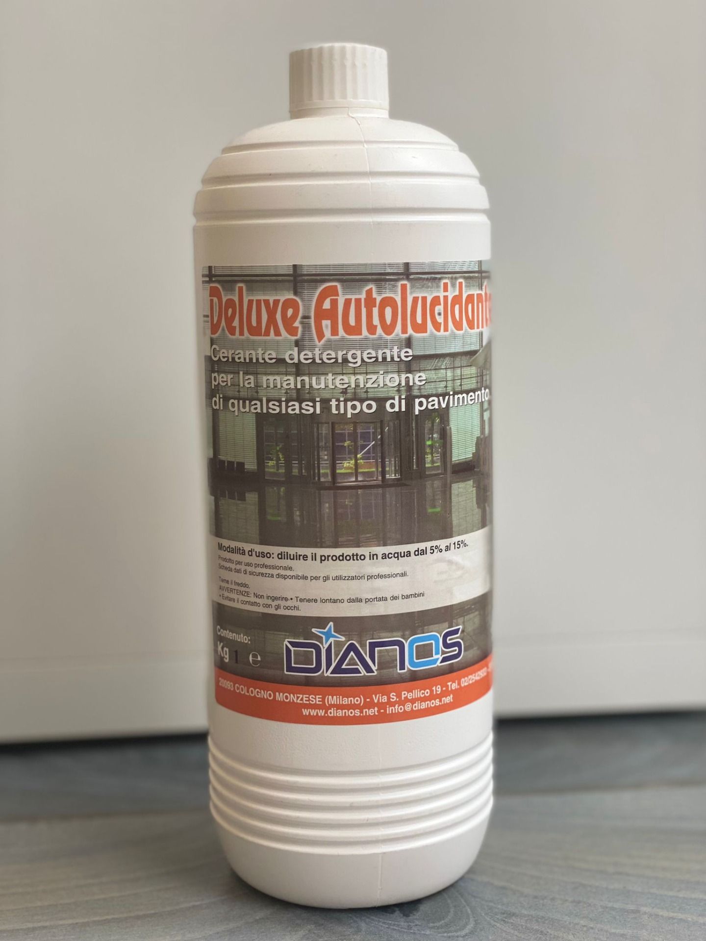 Flacone bianco di detergente autolubrificante Deluxe con etichetta rossa e grigia su sfondo neutro.