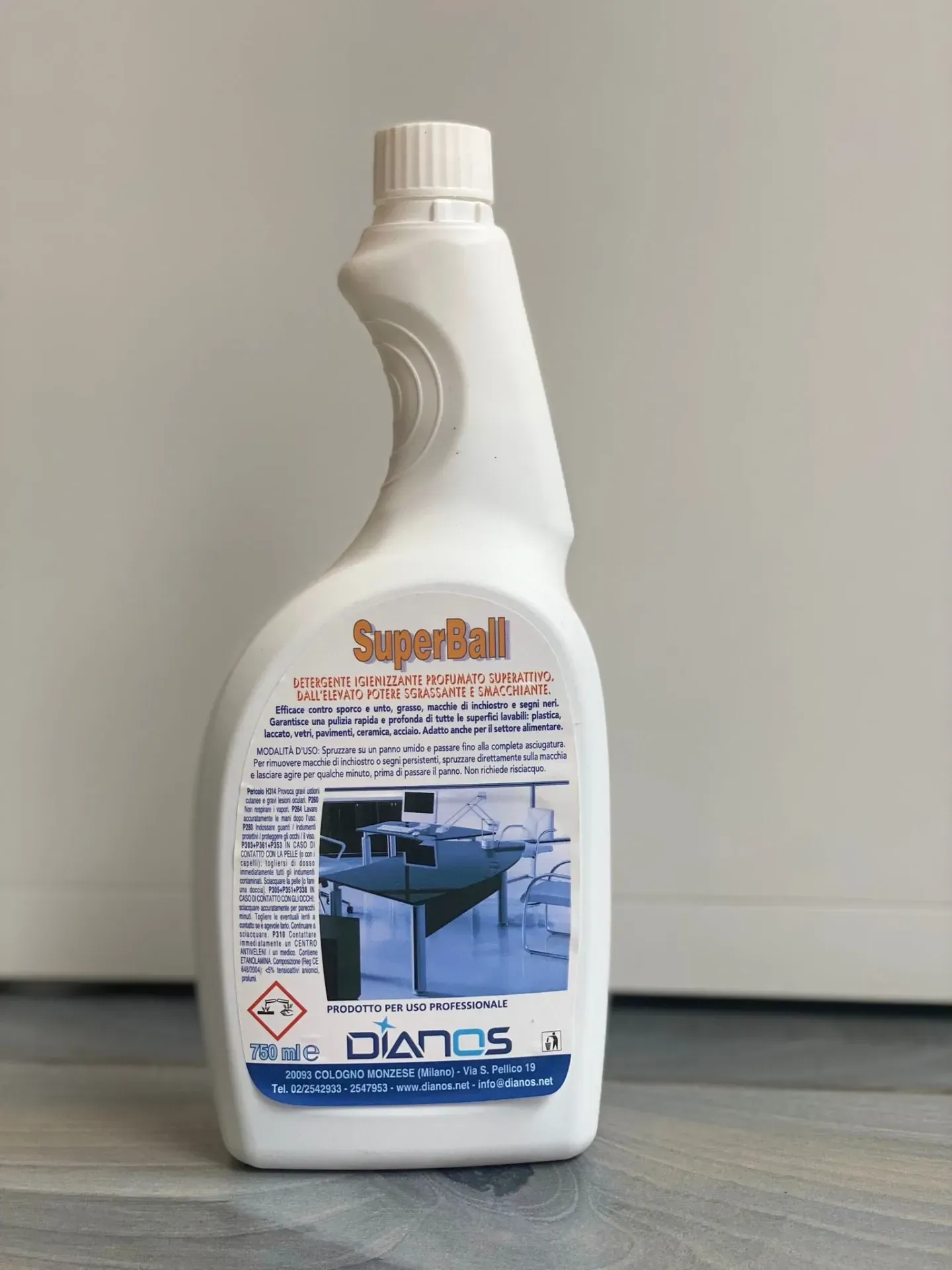 Flacone spray detergente bianco con etichetta blu e erogatore a grilletto su un pavimento grigio.