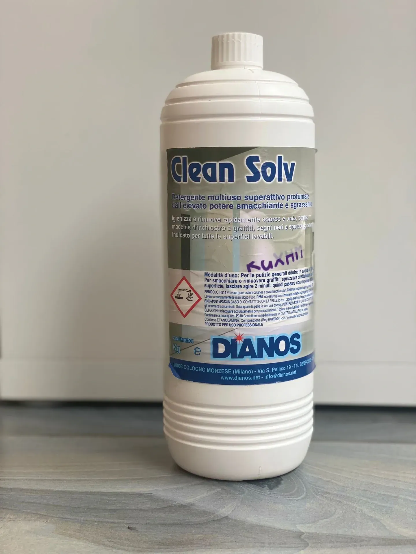 Una bottiglia bianca di detergente Clean Solv è appoggiata su una superficie grigia contro una parete anonima.
