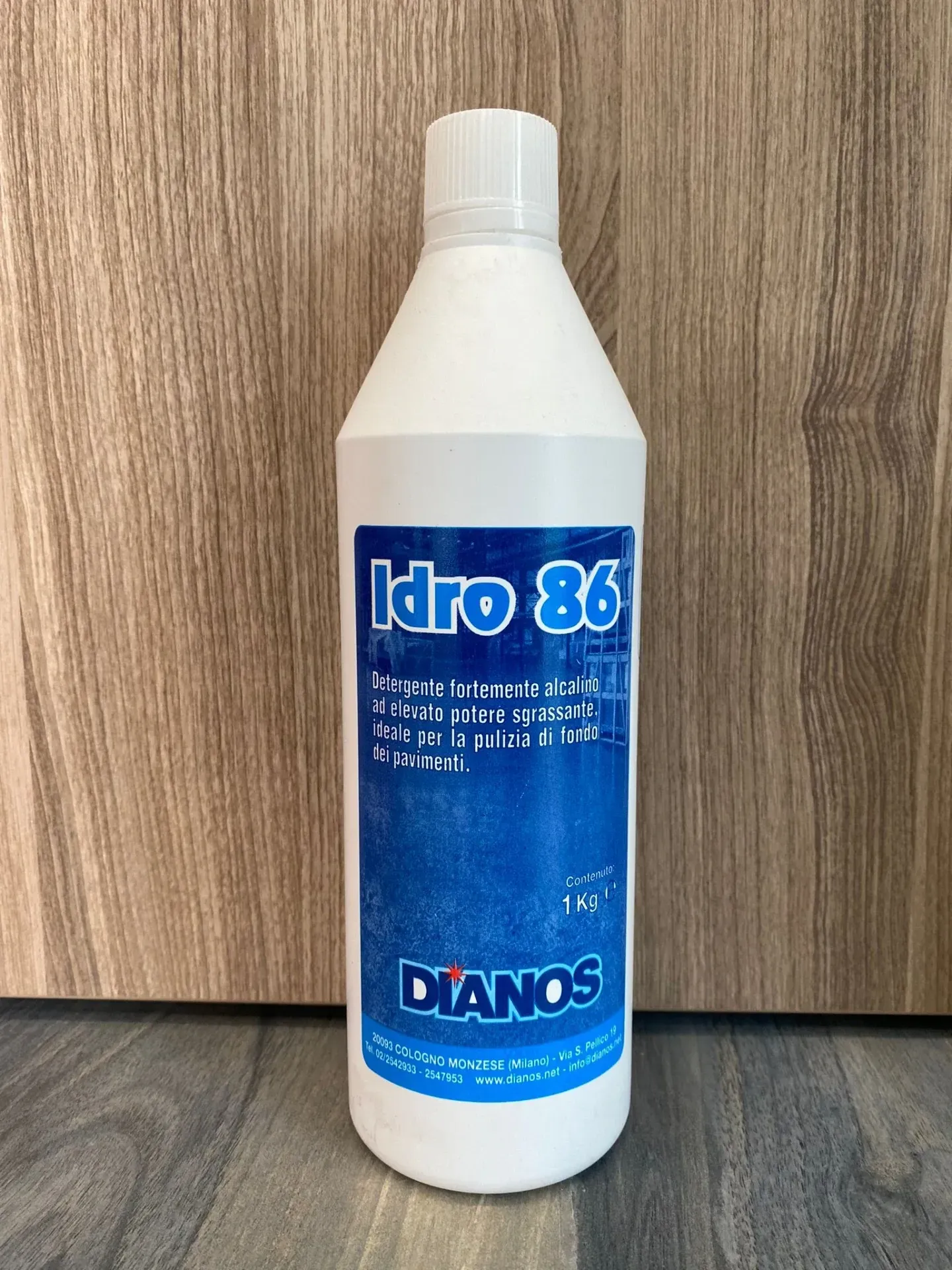 Bottiglia bianca di detergente Idro 86 con etichetta blu, su uno sfondo di legno.