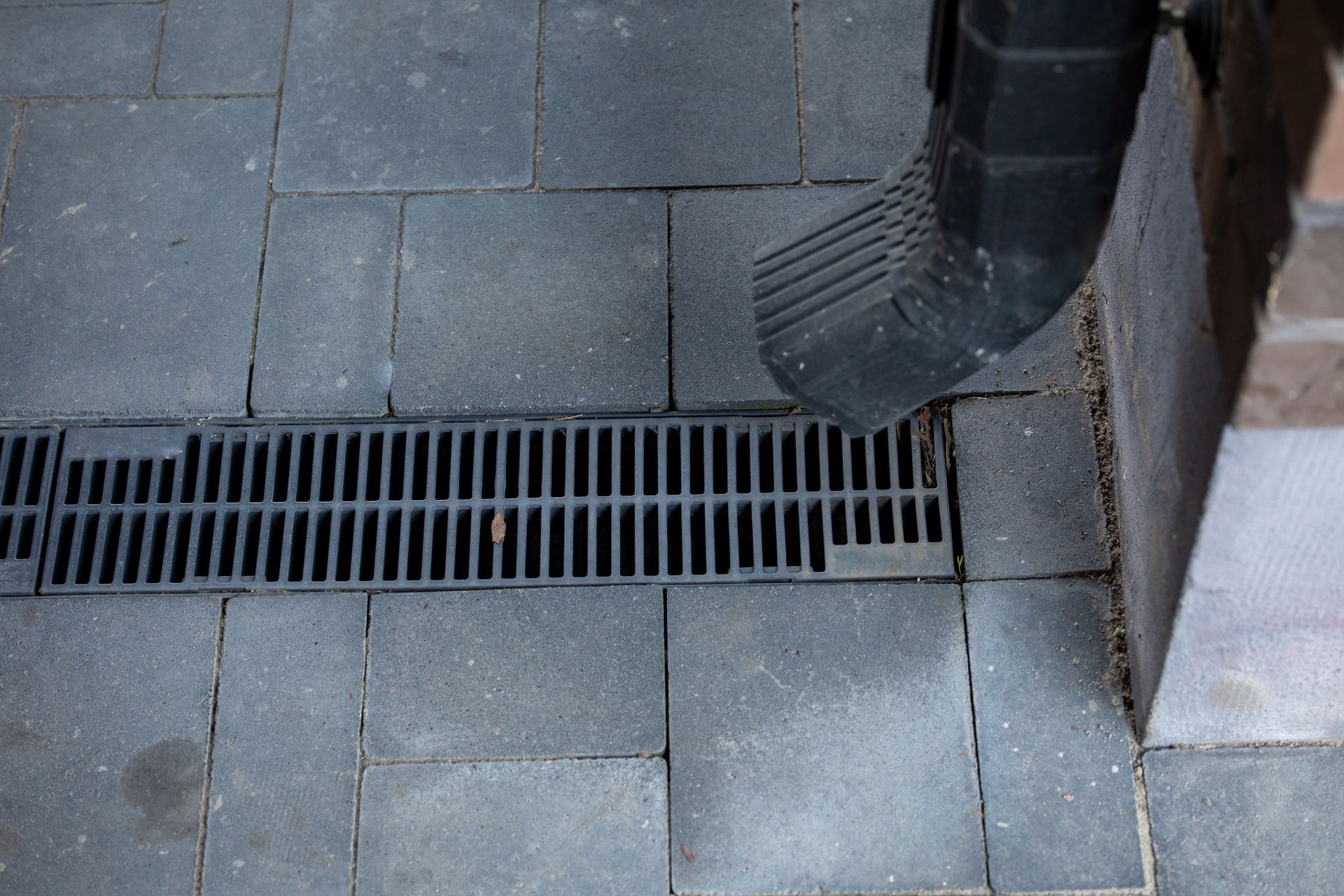 Downspout directing rainwater into a grated drain beside a home's foundation