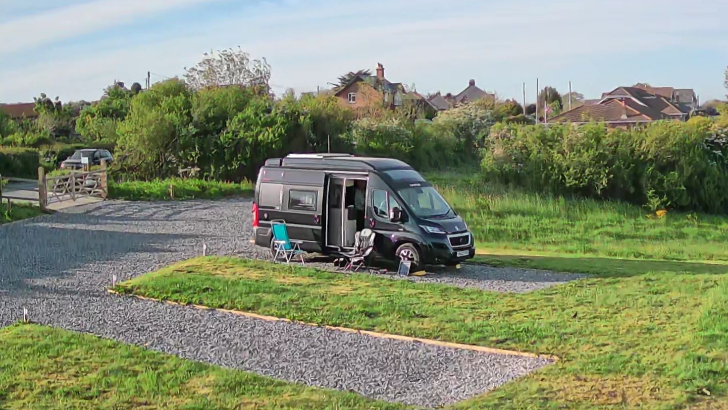 Green camper van with pop-up roof and awning, parked in a field with cows grazing in the background.