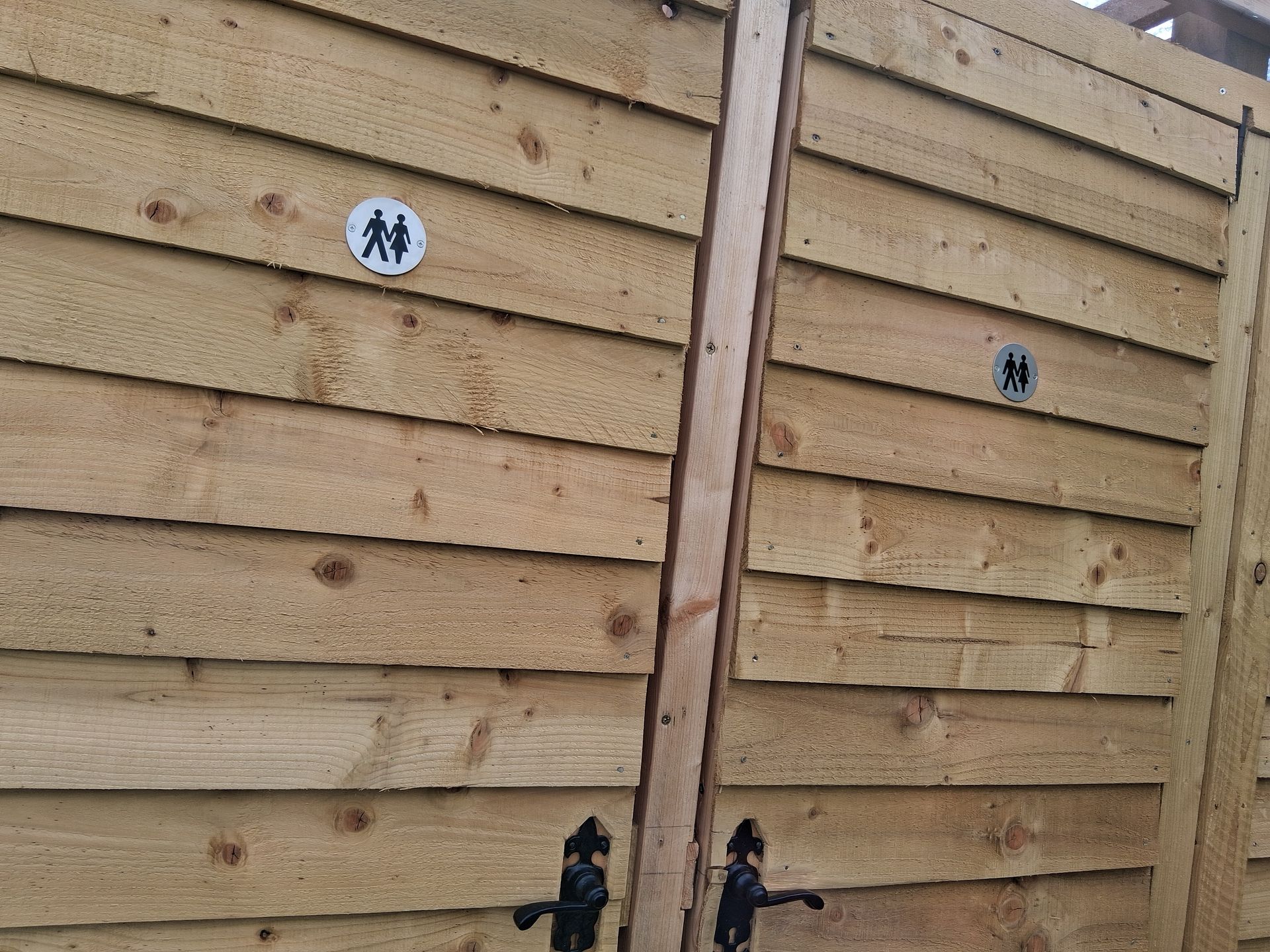Wooden fence with two restroom signs and black gate latches in front