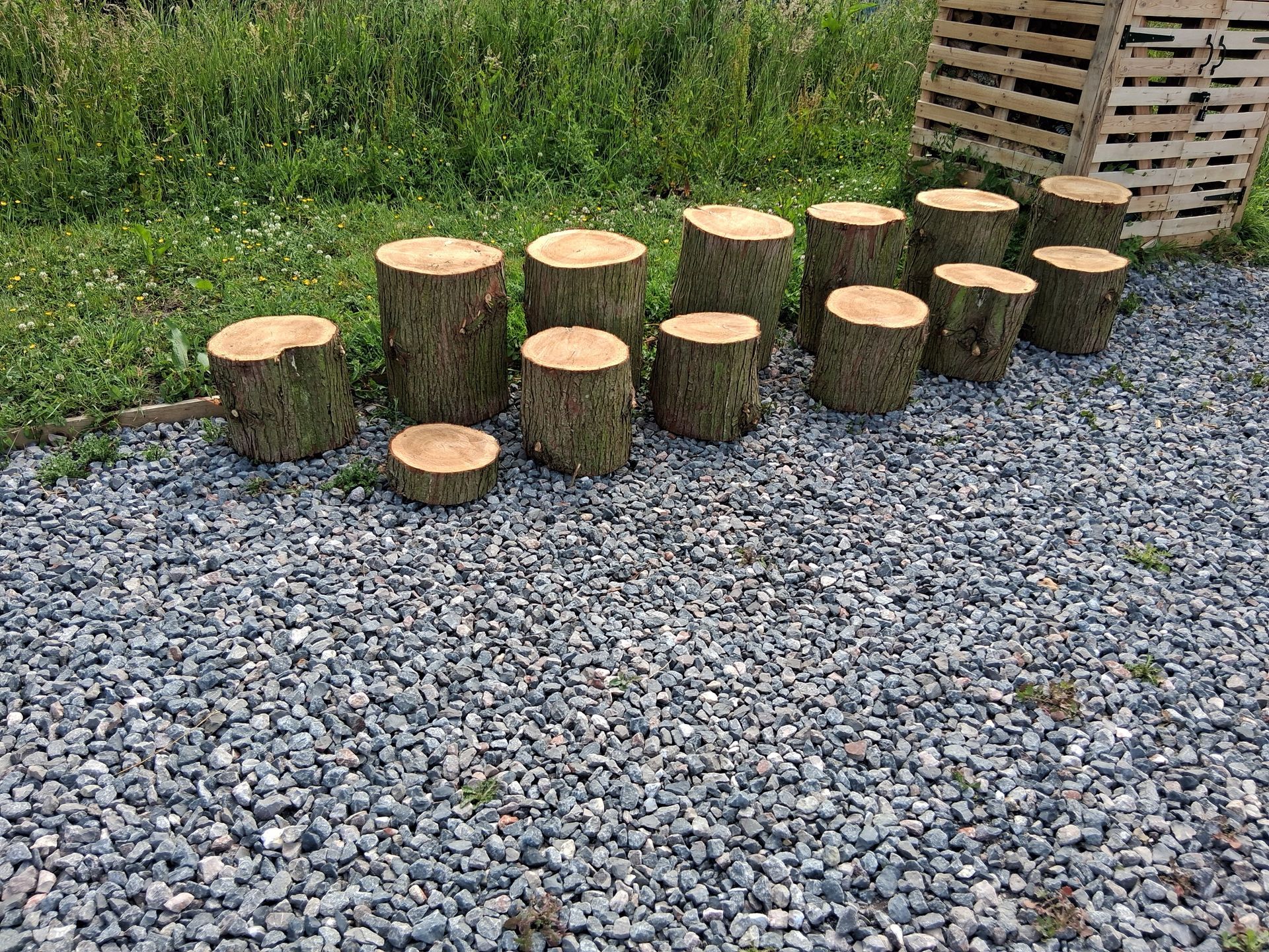 Wooden log stepping stools on gravel beside tall grass, arranged like a small outdoor path