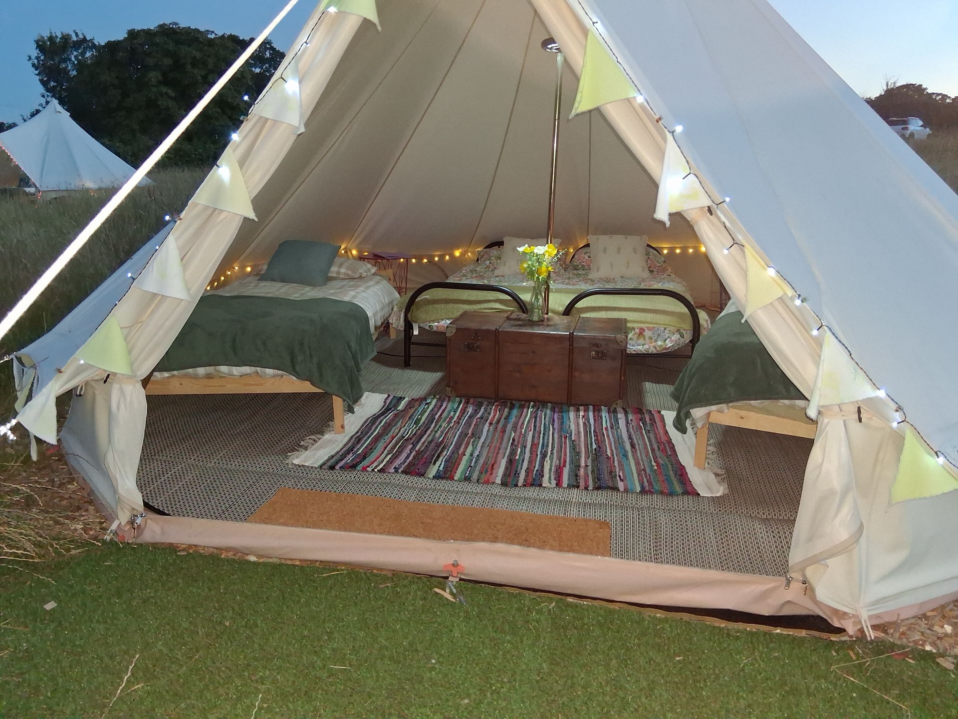 Open canvas tent with rug-covered floor, beds, and lanterns at dusk